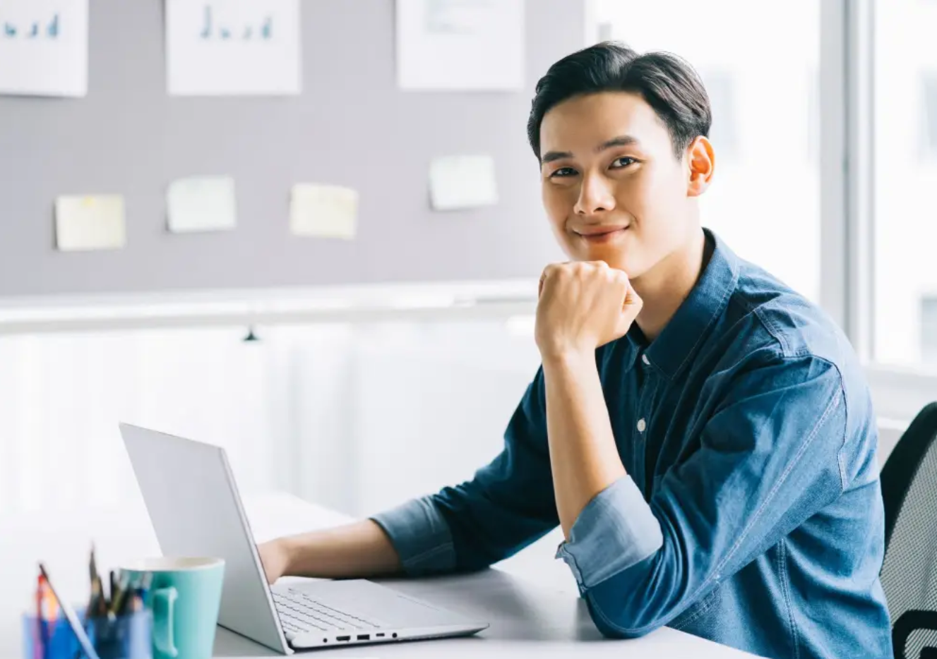 Person seated beside a laptop in a bright workspace.